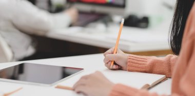 Fikirlerini deftere yazarken projesinde çalışan genç bir kadının yakın plan görüntüsü. 