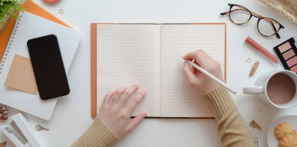 Vista superior de la escritura femenina joven en cuaderno en blanco en concepto de espacio de trabajo femenino beige cálido — Foto de Stock