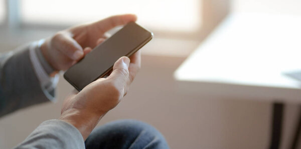 Close-up view of professional businessman looking at his smartphone while working at his workplace