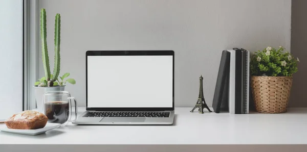 Wygodne miejsce pracy w pobliżu okien z otwartym pustym ekranem laptopa z filiżanką kawy i sprzętem biurowym — Zdjęcie stockowe