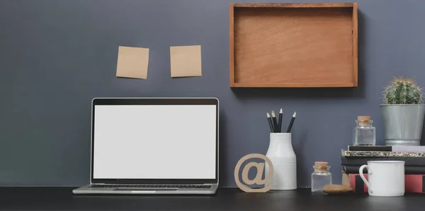 Открытый пустой экран ноутбука в современном рабочем пространстве с украшениями и офисными принадлежностями на черном столе и серой стене — стоковое фото