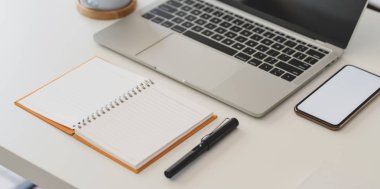 Açık not defteri, dizüstü bilgisayarı ve akıllı telefonu olan rahat bir iş yeri görüntüsü.