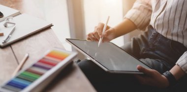 Çalışma odasında ofis malzemeleriyle boş ekran tableti üzerinde çalışan genç profesyonel kadın tasarımcının kırpılmış görüntüleri. 