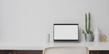 Açık dizüstü bilgisayarı ve beyaz masa ve beyaz duvar zemininde dekorasyonları olan en az çalışma alanı 