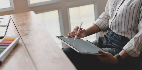 Imagen recortada de una joven diseñadora profesional que trabaja en una tableta de pantalla en blanco en su espacio de trabajo con suministros de oficina — Foto de Stock