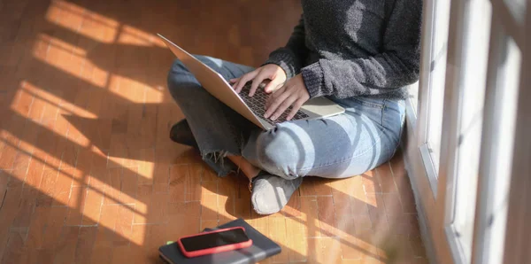 Vista de cerca de la joven freelancer trabajando en su proyecto con computadora portátil mientras está sentada cerca de las ventanas —  Fotos de Stock