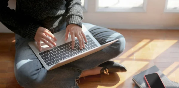 Vista de cerca de la joven freelancer trabajando en su proyecto con computadora portátil mientras está sentada cerca de las ventanas —  Fotos de Stock