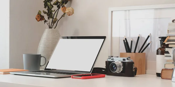 Минимальное рабочее место с ноутбуком, камерой, офисными принадлежностями и вазой для сухих роз на белом столе — стоковое фото