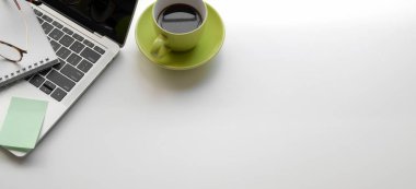 Laptop bilgisayarı ve yeşil kahve fincanı olan modern iş yerinin beyaz masa üzerindeki görüntüsü.