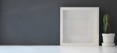 Çerçeveyi kaktüsle modelle modern çalışma alanında beyaz masa ve koyu gri duvar arka planında
