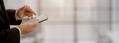 İş adamı bulanık ofis geçmişi olan boş ekran akıllı telefonuna dokunuyor