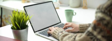Boş ekran laptopuyla çalışan bir kadının görüntüsü. Kahve fincanı ve basit çalışma masası süslemesi.