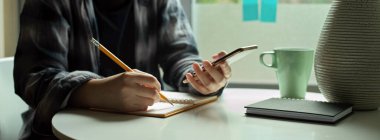 Kadın serbest çalışanın yan görünümü pencereye karar verir ve akıllı telefondan bilgi alırken zaman çizelgesine not alır 