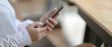 Kafeteryada otururken akıllı telefon kullanan bayan üniversite öğrencisinin yan görüntüsü