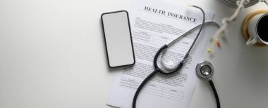 Sağlık sigortası formu, steteskop, sahte akıllı telefon ve beyaz masadaki haplarla ilgili konsept.