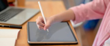 Ödevini hazırlayan bayan üniversite öğrencisinin kütüphane masasındaki tablet, dizüstü bilgisayar ve kırtasiye malzemeleriyle yan görünüşü 