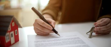 Ev kredisi sözleşmesi imzalayan bir kadının ev modelinin olduğu beyaz masanın üzerinde evinin anahtarını tutarken yakın plan görüntüsü 