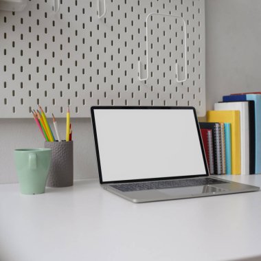Boş ekran bilgisayarı, kupası, kırtasiyesi ve beyaz masadaki kitaplarıyla şık bir ev ofisinin kırpılmış görüntüleri.