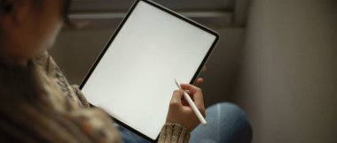 Kolejli genç bir kızın köşe başında otururken stilus kalemle dikey tablet kullanırken görüntüsü kesilmiş. 