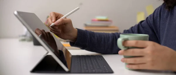 女性员工用手写笔在数字平板电脑上书写并将咖啡杯放在写字台的侧视图 — 图库照片