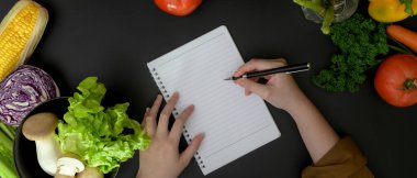 Bayan öğrencinin karanlık, modern mutfak odasındaki boş not defterine yemek tarifi aldığı bir fotoğraf. 