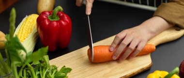 Kadın aşçının karanlık modern mutfakta taze havuç dilimleyişini yakından izleyin. 