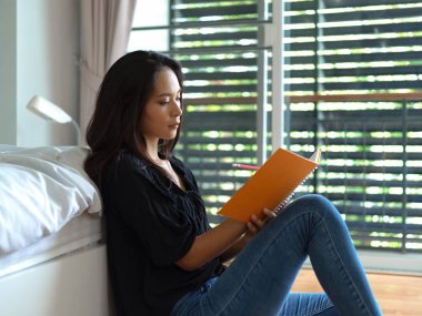 Yatak odasında yerde otururken ajandasına yazı yazan kadın serbest yazar.