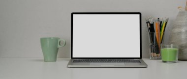 Boş ekran dizüstü bilgisayar, kırtasiye, kupa, süsleme ve beyaz masa üzerine kopyalama alanı ile basit çalışma alanı görünümünü kapat