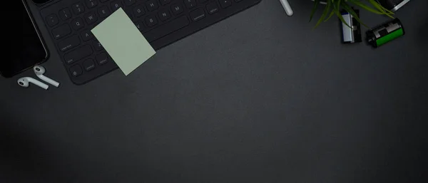 Top view of dark modern workspace with copy space, wireless keyboard with notepad and decorations