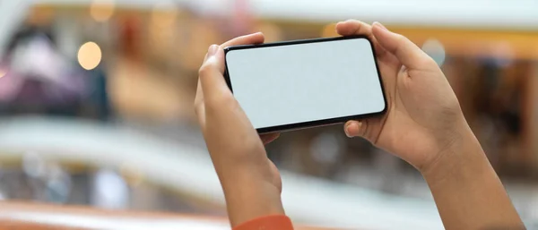 Close up view of a girl holding horizontal mock-up smartphone while standing at balcony in shopping mall