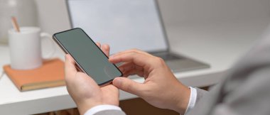 Beyaz ofis masasında ofis malzemeleriyle otururken, erkek girişimci ellerinin akıllı telefon kullanarak görüntüsünü kapat 