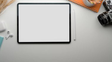 Boş ekran tableti, çay fincanı, kamera, kırtasiye ve kablosuz kulaklık ile modern çalışma tablosunun üst görünümü