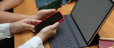 Kütüphanede tabletle çalışırken projeleri için bilgi toplamak amacıyla akıllı telefondan internette sörf yapan kadın üniversite öğrencilerinin yan görüntüsü 