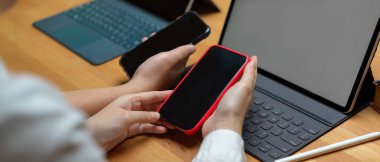 Kütüphanedeki ahşap masada tabletle çalışırken akıllı telefondan bilgi paylaşan kadın üniversite öğrencilerinin yan görünüşü 