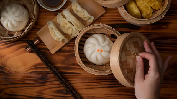 Overhead shot of female hand opening bamboo seamer to eat steamed pork buns and dumplings  in Chinese restaurants