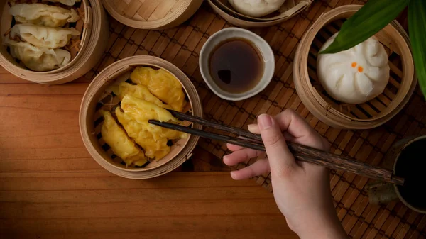 Overhead shot of female hand with chopsticks ready to eat steamed dumplings serving on bamboo seamer in Chinese restaurants