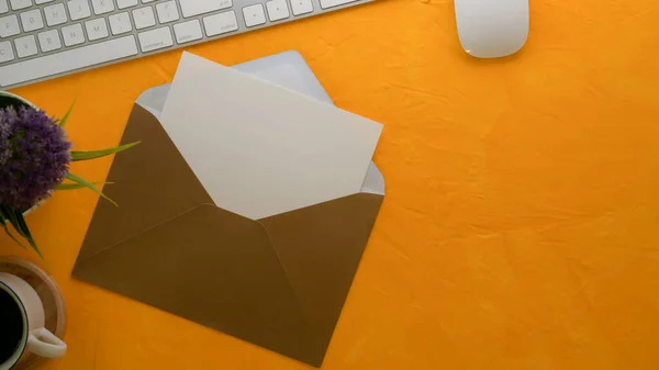 Top view of open mock-up greeting card with brown envelope on creative worktable with computer keyboard, decoration and copy space