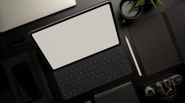 Ofis malzemeleri, kamera ve dekorasyonla birlikte karanlık ofis masasında klavyeli boş ekran tableti üst görünümü