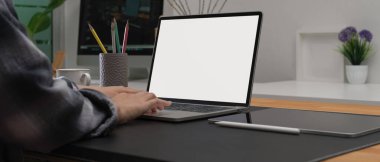 Kadın tasarımcının ofis masasında oturup ofis odasında dizüstü bilgisayar ve diğer malzemelerle çalışırken çekilmiş görüntüsü. 