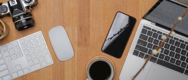 Laptop, kablosuz bilgisayar aygıtları, akıllı telefon, kamera ve kahve fincanı ile modern çalışma alanının en üst görünümü 