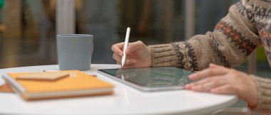 İnternette, oturma odasındaki sehpanın üzerinde tablet ve kırtasiye malzemeleriyle öğrenen bayan üniversite öğrencisinin yan görüntüsü.