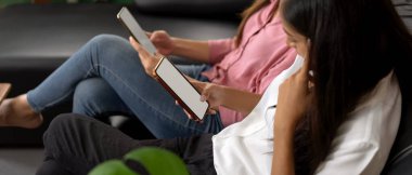 Siyah kanepede oturan ve oturma odasında sahte akıllı telefon kullanan genç bir kız resmi. 