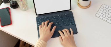 Beyaz ofis masasında akıllı telefon ve malzemelerle birlikte klavye ile sahte tablet yazan bir kadın resmi.