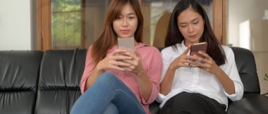 Siyah kanepede oturan ve oturma odasında akıllı telefon kullanan iki genç kızın portresi.