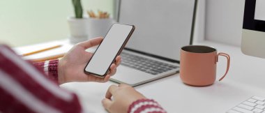 Beyaz masadaki sahte akıllı telefon kullanarak dizüstü bilgisayar, kupa ve süsleme ile kadın görüntüsünü kapat