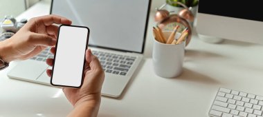 Ofis masasında laptop ve ofis malzemeleriyle akıllı telefon kullanan bir erkeğin görüntüsünü kapat.