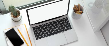 Çalışma köşesinin üst görüntüsü dizüstü bilgisayar, akıllı telefon, kırtasiye ve dekorasyon ile beyaz masa üzerinde