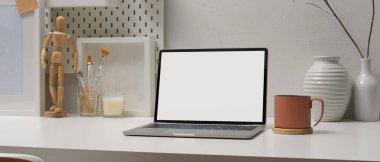 Bilgisayarı, fırçaları, bardakları ve süslemeleri beyaz masanın üzerine çizerek modern çalışabilir.