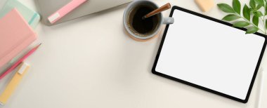 Tablet, laptop, kırtasiye malzemesi, kahve fincanı, dekorasyon ve fotokopi masasıyla kadınsı çalışma masasının üst görünümü 
