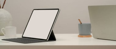 Beyaz masadaki boş ekran tableti, laptopla ve çalışma alanındaki kahve fincanlarıyla kırpılmış.